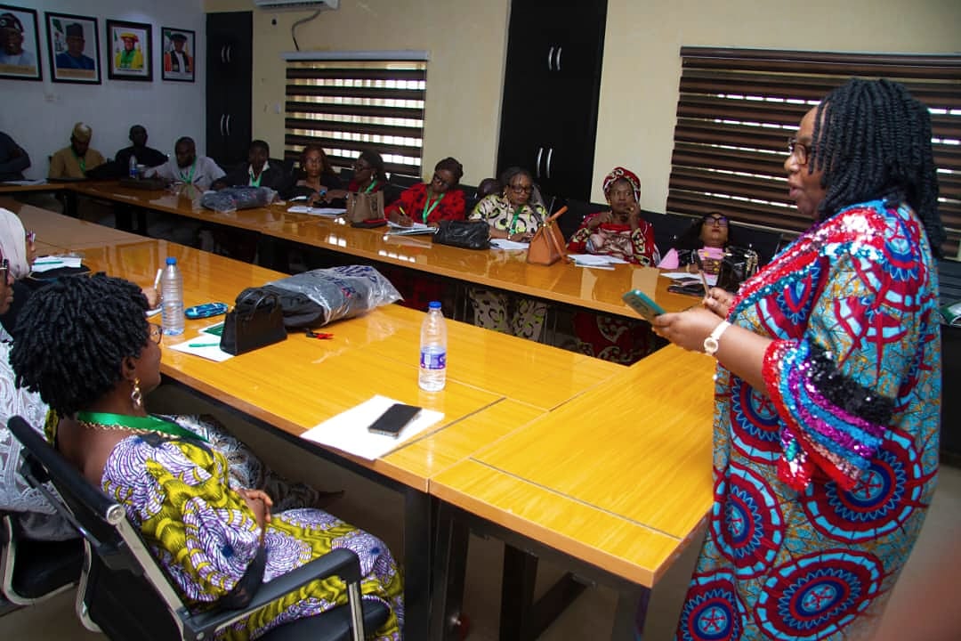 A woman standing and addressing colleagues seated around a boardroom table.