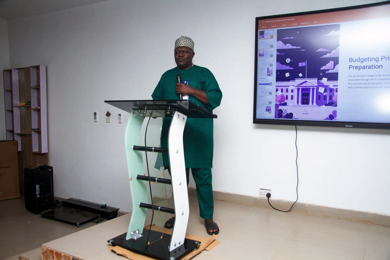 A facilitator presenting beside a screen showing a slide on budget preparation.